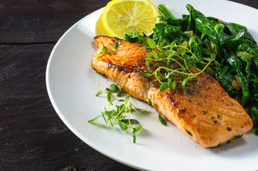 grilled salmon with thyme, lemon and spinach on a white plate on dark wood