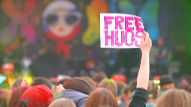 young girl holds free hugs poster at concert and dance