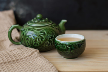 Green tea in a small cup and teapot on wooden background with kitchen towel, chinese tea ceremony set