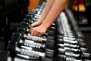 Fototapeta na wymiar female hands close up taking dumbbells from row of barbells in a gym