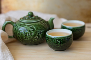 Fresh green tea in two small cups and teapot with traditional chinese ornaments, wooden table
