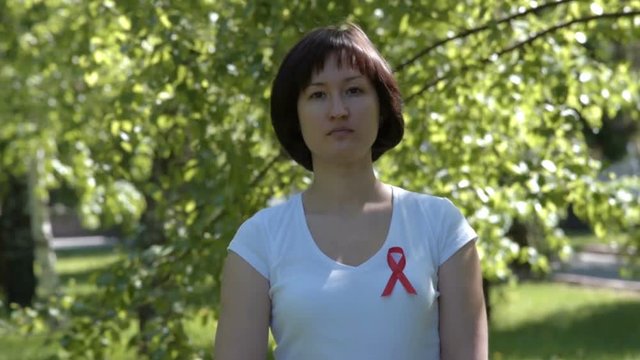 Woman pinning orange ribbon on white t-shirt, green nature background. AIDS and HIV awareness, heart disease, lymphoma, tuberculosis, substance-abuse, vasculitis