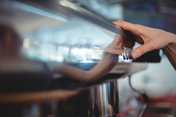 Close-up of barista pushing button on coffee maker at cafeteria