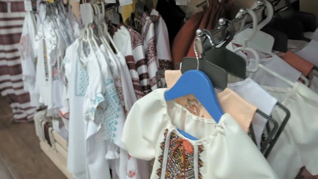 A neat display of fashionable blouses hanging according to the color on the rack. Store contains floral vest with fur border and hand mittens in neutral colors. 4K UHD video footage.