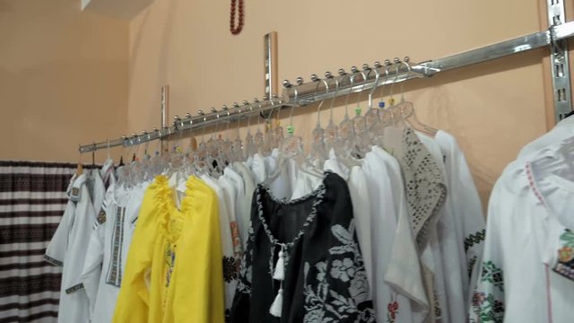 A neat display of fashionable blouses hanging according to the color on the rack. Store contains floral vest with fur border and hand mittens in neutral colors. 4K UHD video footage.