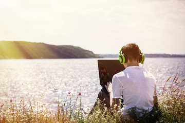 Fototapeta premium teenager working at the computer on the river bank
