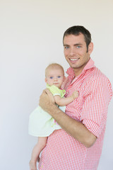 Indoor portrait of young smiling father hugging his little daughter