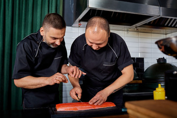 Two chefs cook salmon in the kitchen.