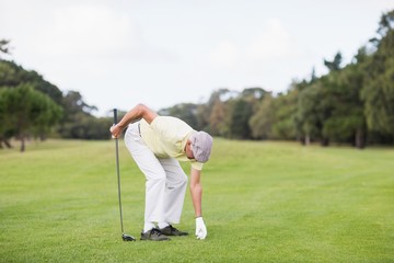 Mature man holding golf club while bending