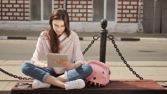 Young beautiful student girl using a tablet computer outside. Pretty teen woman reading on air.