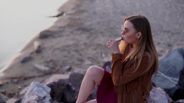 Young beautiful woman smoking ( vaping ) e-cigarette on a sunset beach