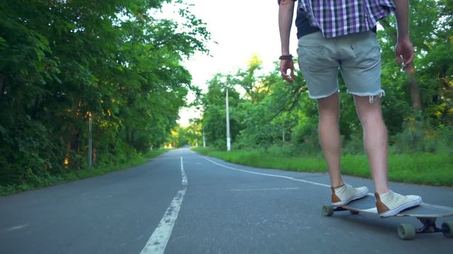back view male riding longboard in the park slow motion