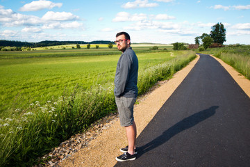 Young attractive man is standing on the bike path through the fi
