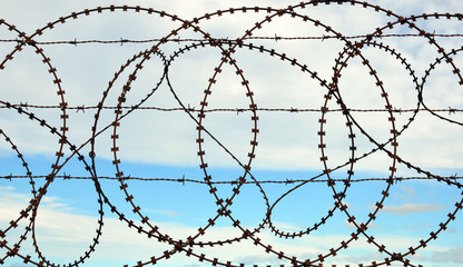 Patterns in a tangled barbed wire fence with sky background
