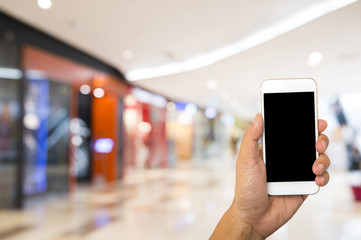 Fototapeta na wymiar Hand hold blank smartphone on blur supermarket background