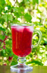 a glass of red cherry juice with ice cubes on a natural background closeup