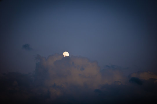 full moon hiding behind the clouds at night