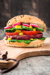 Veggie beet burger with lamb's lettuce, tomato, radish and cucumber on rustic wooden background


