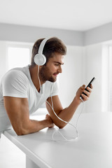 Music Listening. Man In Headphones Using Mobile Phone Indoors