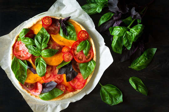 Homemade tart with rikotta, raw tomatoes and basil on black wooden background