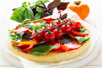 Homemade tart with rikotta, raw tomatoes and basil on white wooden background