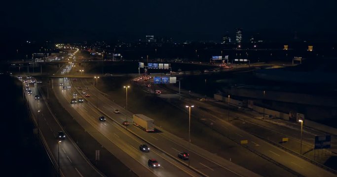 Rear aerial view over O ring traffic with cityscape at night time
