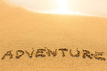 Adventure - word drawn on the sand beach with the soft wave.