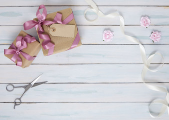 Gift wrap - Presents wrapped in brown parcel paper with pink silk bows, blank tag, pink roses, white ribbon and scissors on a painted wooden table top background forming a page border