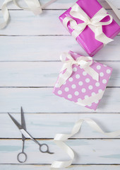 Gift wrap - Presents wrapped in pink wrapping paper with white silk ribbon bows and scissors, on a rustic painted wooden table top background forming a page border