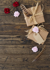Gift wrap - Presents wrapped in brown parcel paper with raffia bows, blank tag, red and pink roses and feathers on a rustic wooden table top background forming a page border