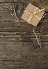 Gift wrap - Present wrapped in brown parcel paper with raffia bow and feathers on a rustic wooden table top background forming a page border