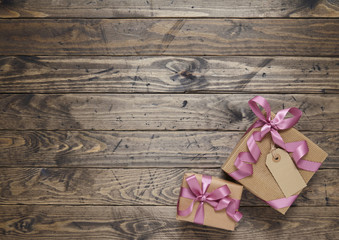 Gift wrap - Presents wrapped in brown parcel paper with pink silk ribbon bows and blank tag on a rustic wooden table top background forming a page border