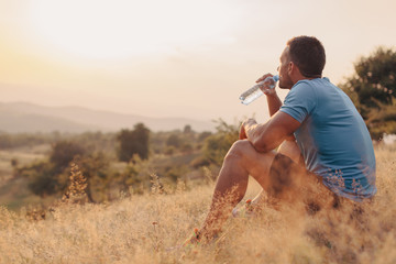 Athletic man in his 30s resting and drinking water from a bottle while sitting down outdoor - Powered by Adobe