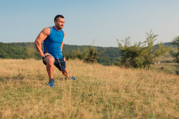 Attractive athletic man in his 30s stretching his legs outdoor preparing for exercise