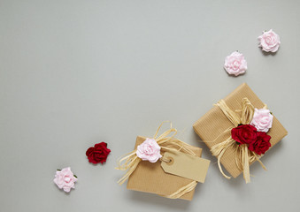 Gift wrap - Presents wrapped in brown parcel paper with raffia bows, a blank label and pink and red rose flowers on a grey background forming a page border