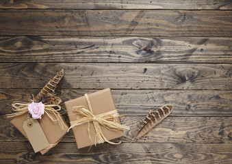 Floral gift wrap - Presents wrapped in brown parcel paper with rustic raffia bows, gift tag, pink rose flowers and feathers, on a distressed wooden tabletop background forming a page border