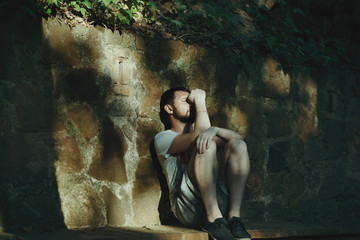 Handsome young man in a European city, sitting on a stone bench and thinks sad