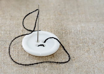 Needle with black thread and white sewing button.