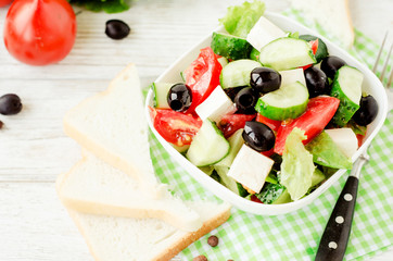 
useful dietary breakfast or lunch , Greek salad with fresh vegetables , tomatoes, cucumbers , lettuce, black olives , feta cheese and white toast on a wooden background