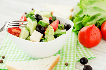 
useful dietary breakfast or lunch , Greek salad with fresh vegetables , tomatoes, cucumbers , lettuce, black olives , feta cheese and white toast on a wooden background