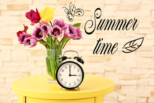 Alarm clock with tulips bouquet and text Summer time on light background