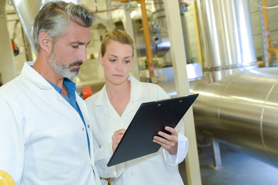 Man and lady in factory looking at clipboard