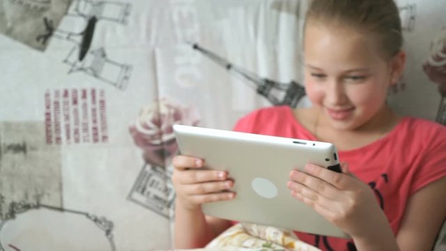 Child reading a digital tablet lying on the bed