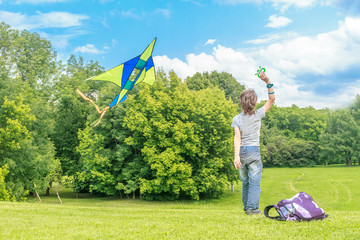 young happy child boy playing with bright kite in park. summer h