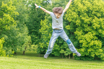 Fototapeta na wymiar Adorable young child boy in the park. On warm summer day during school holidays. Kid boy jumping and smiling.