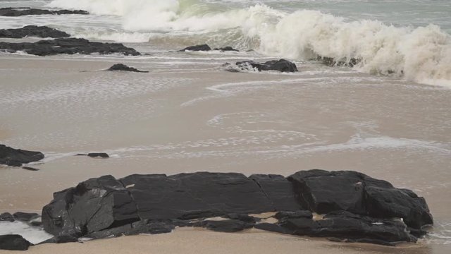 Waves on rocky and sandy beach. Slow motion video shot on cloudy day
