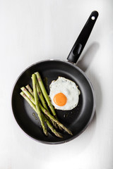 Green asparagus with fried egg on the frying pan