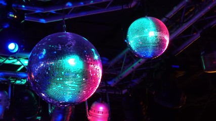 Decorative mirrored balls spin and reflect colorful teal and pink light around concert stage area in dark club.
- Powered by Adobe