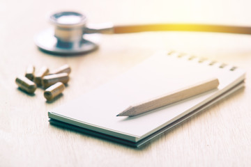 Stethoscope and note book for medical record with medical pills. vintage filter