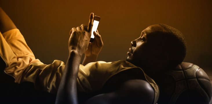 Portrait of basketball player lying and using his smartphone